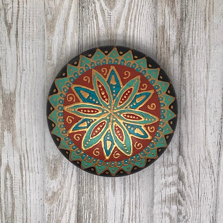 Close-up van een unieke mandala steen in levendige tinten turquoise, rood en goud, afgewerkt met een beschermende laklaag.