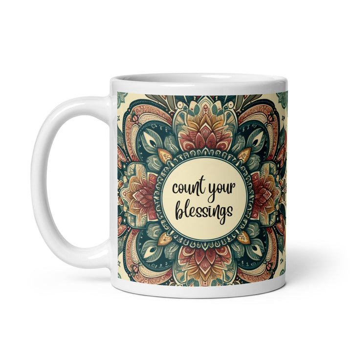 White ceramic mug with a detailed green, red, and gold mandala design and the phrase 'Count Your Blessings' in the center.