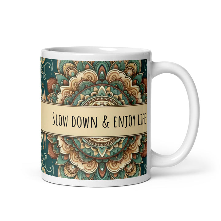 White ceramic mug with a detailed green and beige mandala design and the phrase 'Slow Down & Enjoy Life' in the center.