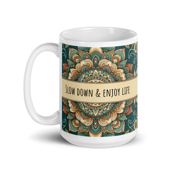 White ceramic mug with a detailed green and beige mandala design and the phrase 'Slow Down & Enjoy Life' in the center.